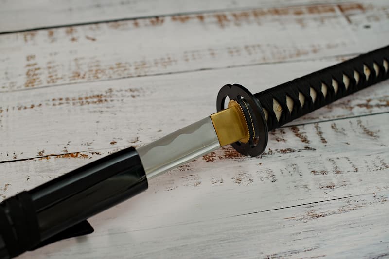 Katana tranchant avec monture noire, tsuba Miyamoto Musashi, livré avec une housse de protection en tissu (version luxe : dans un coffret en bois composite avec un support en bois verni avec protections et un kit d'entretien) | XVIIᵉ siècle, province de Musashi (région de Tōkyō). Forgée par Nagakuni, mon appartenance a été gravée sur ma soie (nakago 茎), discrètement, mais de manière indélébile.