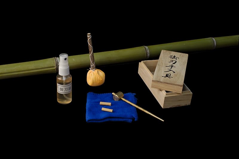 Huile de protection, micro-fibre, boule de craie (Uchiko), chasse goupilles (Mekugi Nuki) et goupilles (Mekugi), livrés dans une boîte en bois | J’ai le privilège d’entretenir les katanas des meilleurs samouraïs. J’en entretiens la lame pour la protéger des attaques de l’oxydation. En effet, les aciers non alliés (sans adjuvants comme le chrome et le molybdène) sont exposés à la rouille. Alliage de fer et de carbone, l’acier est fragilisé par la présence d’oxygène. L’air peut donc l’attaquer et c’est la raison pour laquelle mon huile permet de protéger la surface de ce noble métal.