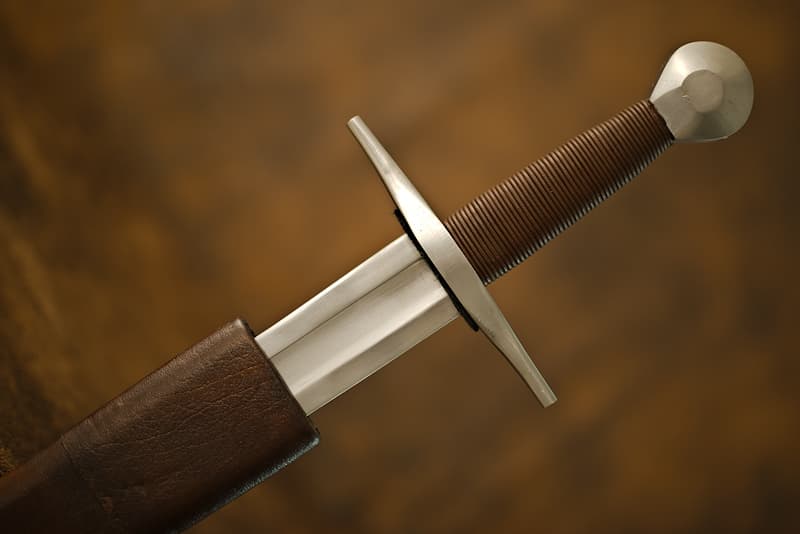 Épée médiévale forgée, lame courte à gorge, poignée recouverte de cuir, pommeau cylindrique, fourreau en bois et cuir