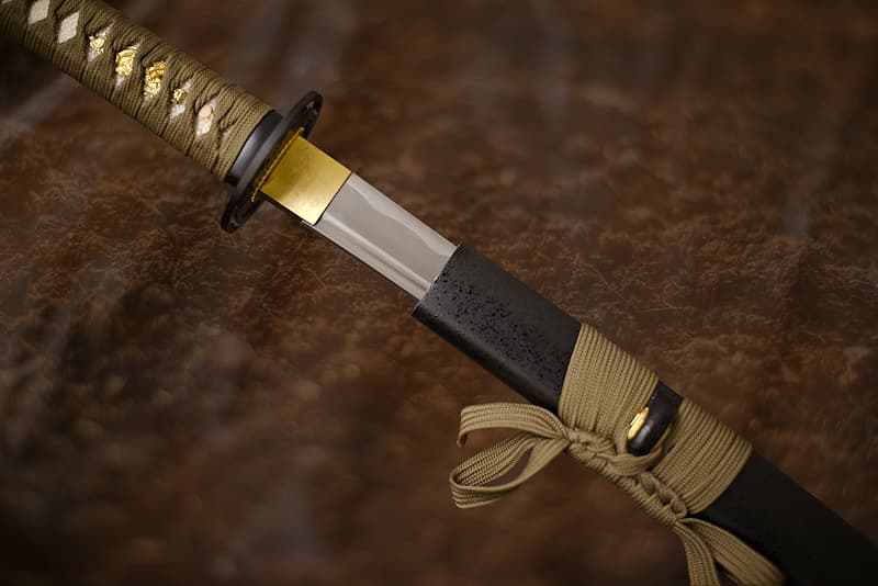 Katana tranchant avec fourreau (saya 鞘) en bois laqué noir avec reliefs (gouttelettes), tressages (tsuka-Ito 柄糸 et sageo 下緒) marron (brun) | La légende raconte que je suis née à partir d’un morceau de terre extrait de la Montagne sacrée, Fujisan (富士山). Le maître forgeron qui m’a donné vie aurait choisi le meilleur minerai pour le transformer, après des semaines de dur labeur en fine lame. Polie, affûtée comme un rasoir, j’ai ensuite été confiée à un samouraï qui participa à la Bataille de Sekigahara (関ヶ原の戦い), en 1600.