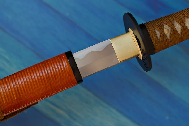 Katana tranchant avec fourreau (saya 鞘) bois, marron et gaine annelée partielle, livré avec une housse de protection en tissu | Le premier samouraï que j’ai servi vivait dans la Province de Kaga (加賀国) au début du XVIIᵉ siècle. Il était au service du clan Maeda, la véritable famille qui gouverna le Japon pendant la période de shogunat des Tokugawa.