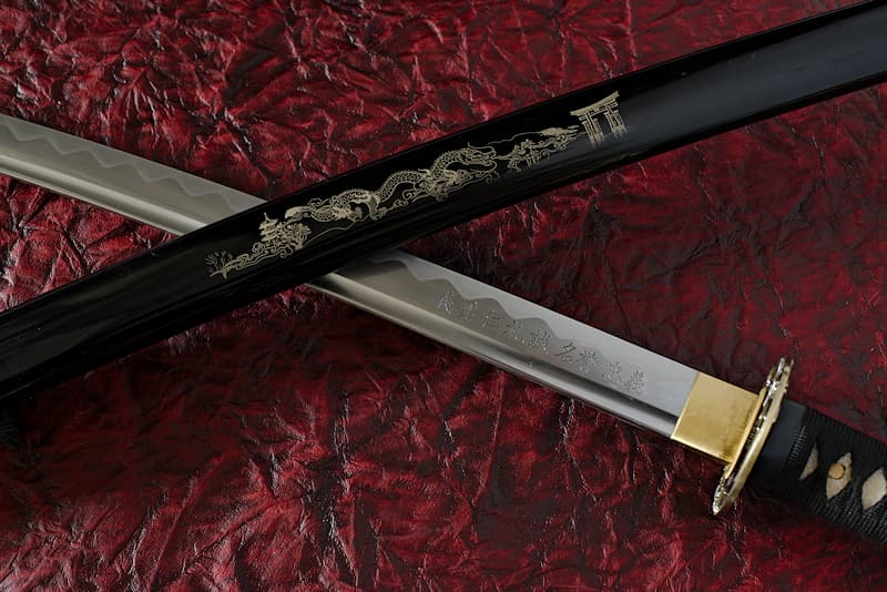 Katana affûté avec fourreau (Saya 鞘) gravé (composition japonaise avec dragon), Tsuka-Ito (柄糸) et Sageo (下緒) noirs, lame gravée (les 7 vertus du Bushidō), livré avec une housse de protection en tissu, dans un coffret en bois composite avec un support en bois verni avec protections et un kit d'entretien | J’incarne les valeurs des samouraïs. Les gravures que je porte représentent les sept valeurs fondamentales qu’Inazō Nitobé a attribuées à la Voie du guerrier, le Bushidō (武士道) : la droiture, le courage, la bienveillance, la politesse, la sincérité, l’honneur et la loyauté.