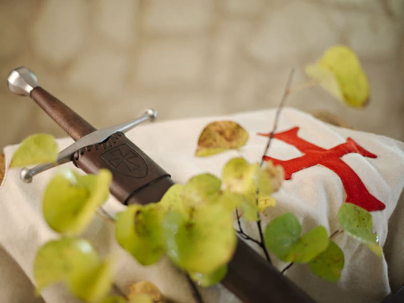 Épée médiévale forgée, posée sur un tabard blanc en laine arborant la croix pattée des templiers