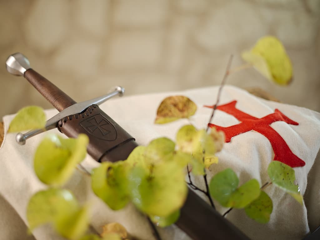Épée médiévale forgée, posée sur un tabard blanc en laine arborant la croix pattée des templiers