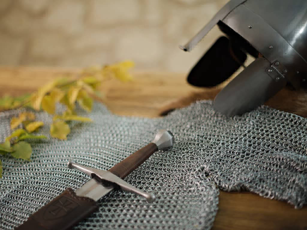Casque médiéval posé sur sur une table tréditionelle, avec une cotte de maille et une épée médiévale de frappe