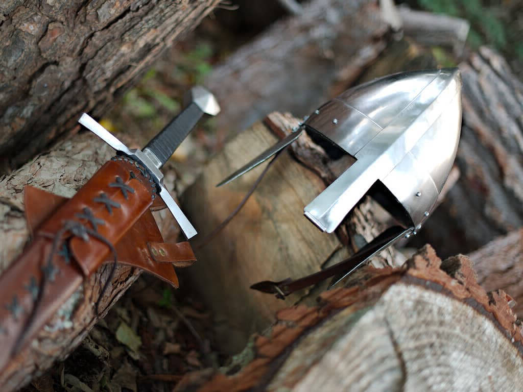 Casque et épée médiévale posés sur des bûches en bois en pleine forêt enchantée