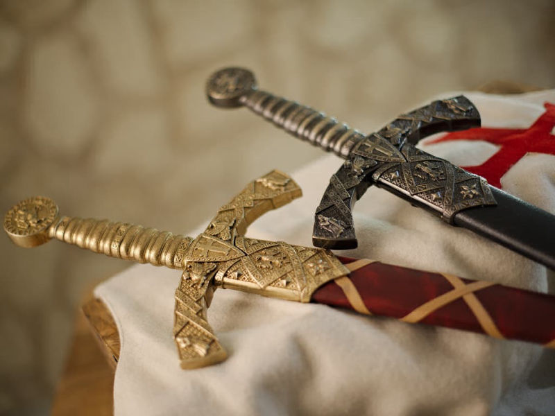 Les deux épées templières de décoration avec fourreau rouge tressé ou noir, posées sur un tabard templier blanc en laine, arborant la croix pattée rouge templière Les deux épées templières de décoration avec fourreau rouge tressé ou noir, posées sur un tabard templier blanc en laine, arborant la croix pattée rouge templière