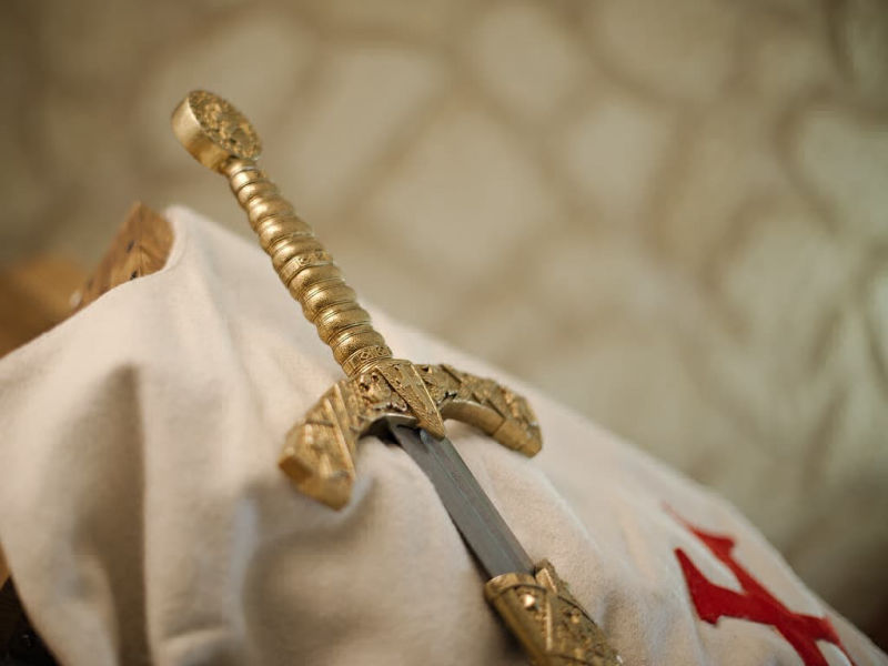 Mise en scène de l'épée templière de décoration avec fourrreau rouge tressé, posée sur un tabard templier blanc arborant la croix pattée rouge templière Mise en scène de l'épée templière de décoration avec fourrreau rouge tressé, posée sur un tabard templier blanc arborant la croix pattée rouge templière