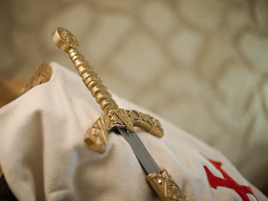 Mise en scène de l'épée templière de décoration avec fourrreau rouge tressé, posée sur un tabard templier blanc arborant la croix pattée rouge templière Mise en scène de l'épée templière de décoration avec fourrreau rouge tressé, posée sur un tabard templier blanc arborant la croix pattée rouge templière