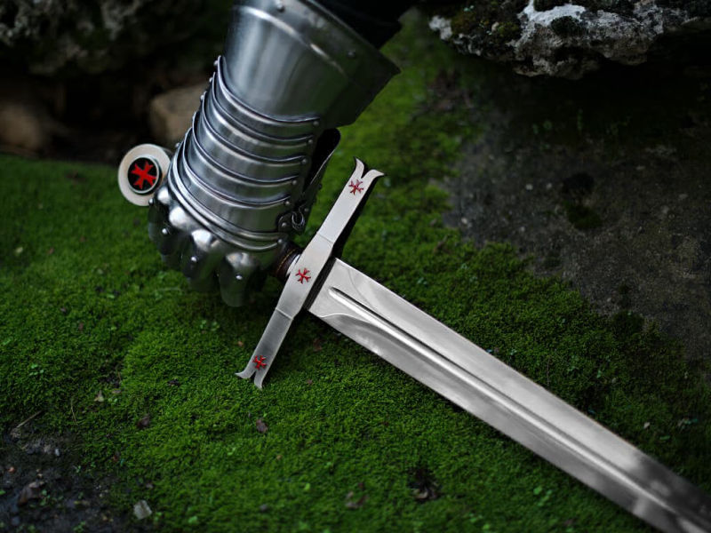 Une main protégée d'un gantelet médiéval prend possession de l'épée templière de décoration Une main protégée d'un gantelet médiéval prend possession de l'épée templière de décoration