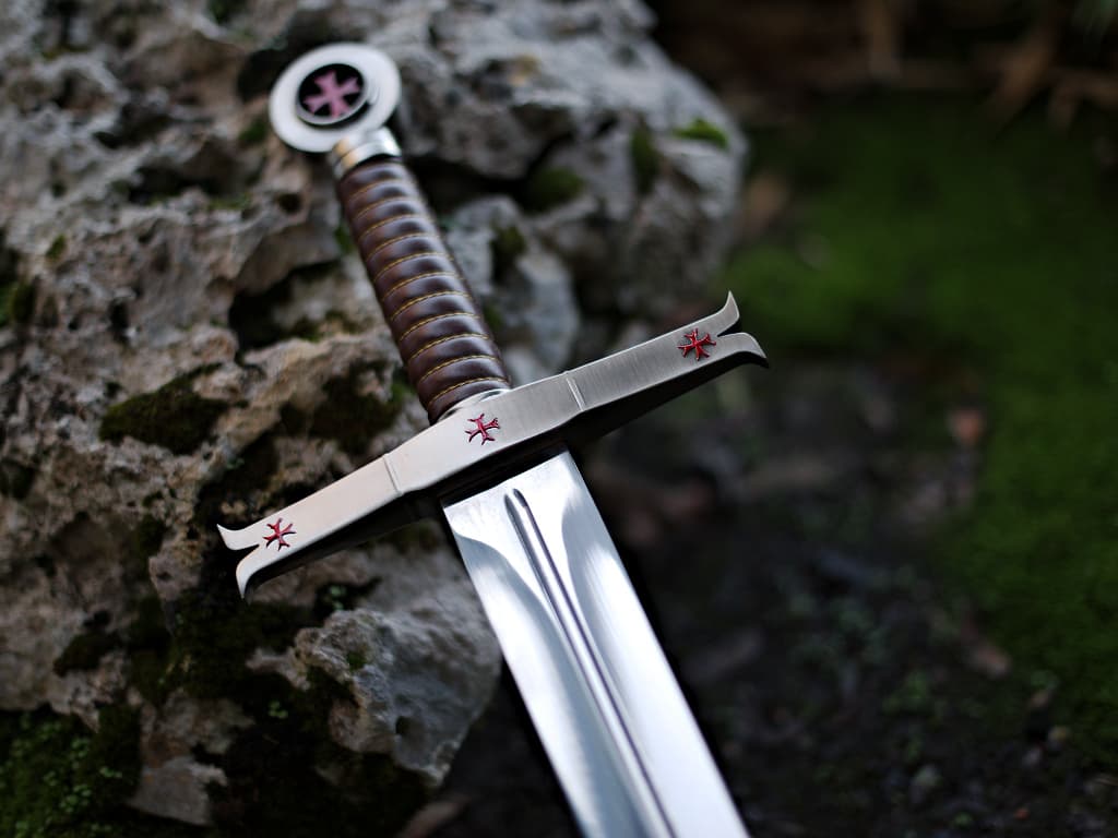 Épée templière de décoration posée sur un rocher avec un arrière-plan en mousse végétale Épée templière de décoration posée sur un rocher avec un arrière-plan en mousse végétale