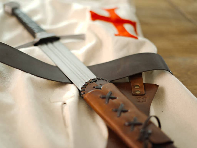 Tabard templier avec épée de combat posés sur une table médiévale en bois Tabard templier avec épée de combat posés sur une table médiévale en bois