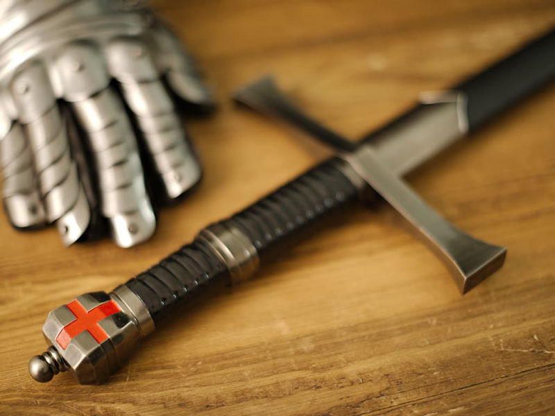 Épée templière de décoration posée sur une table médiébale en bois, avec une branche dont les branches abritent des gouttes de rosée Épée templière « Retour de Terre Sainte » #Terressens